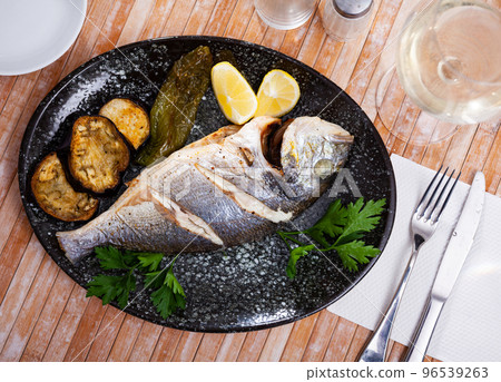 Grilled dorada with baked eggplant and pepper, fresh lemon and greens 96539263