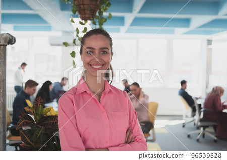 Portrait of young smiling business woman in creative open space coworking startup office. Successful businesswoman standing in office with copyspace. Coworkers working in background. 96539828