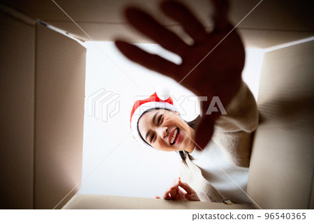 Happy young asian woman wearing christmas hat and unpacking gift box Happy young asian woman wearing christmas hat and unpacking gift box 96540365