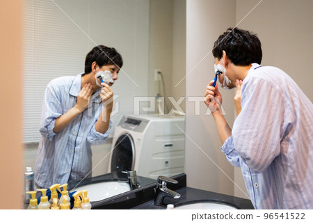 一個 40 多歲的男人用 T 形剃須刀剃須 96541522