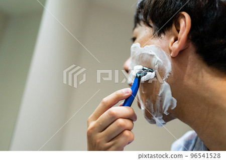 一個 40 多歲的男人用 T 形剃須刀剃須 96541528
