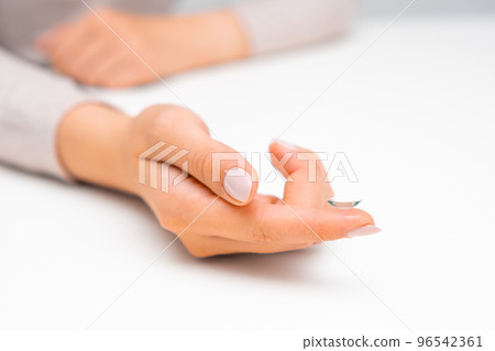 Woman hand holding eye contact on the white surface. Woman hand holding eye contact on the white surface. 96542361