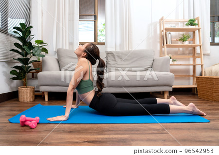 Young woman is practicing yoga with cobra pose during exercise on mat in her living room at home 96542953