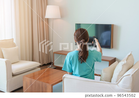 Woman relaxing on the couch, Girl using remote control and choosing TV show and movie series during rest on sofa in the morning. Apartment living concept 96543502