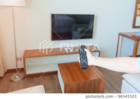 hand using remote controller for adjust Smart TV inside the modern room at home. Apartment living concept 96543503