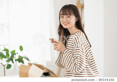 一位年輕女性使用智能手機應用程序出售不必要的物品 一位年輕女性使用智能手機應用程序出售不必要的物品 96544198