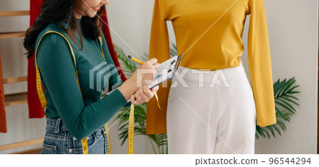 The designer is measuring the shirt fashion working on her designs in the studio.. The designer is measuring the shirt fashion working on her designs in the studio.. 96544294