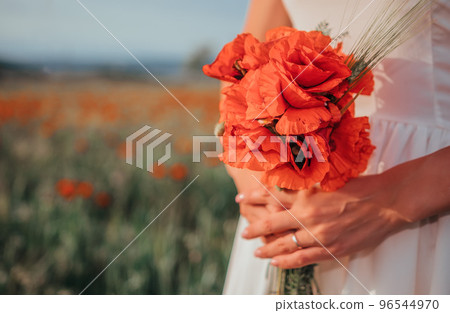 Bride in a white dress holding a bouquet of poppy flowers, warm sunset time on the background of the red poppy field. Copy space. The concept of calmness, silence and unity with nature. Bride in a white dress holding a bouquet of poppy flowers, warm sunset time on the background of the red poppy field. Copy space. The concept of calmness, silence and unity with nature. 96544970