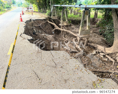 Asphalt road collapsed and cracks in the roadside, Road landslide subside with road cone caused by river erosion 96547274
