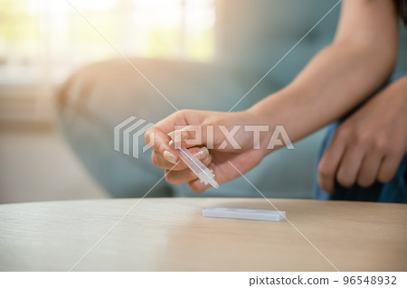 Close up woman hands using rapid antigen test kit for selftest, female four drops of liquid to perform fast coronavirus ATK self test at home in living room on sofa after lockdown and Home Isolation 96548932