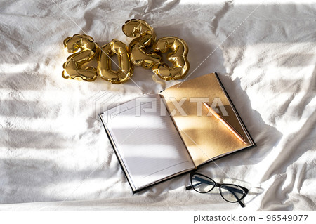 2023 New year goals concept. Blank open notebook and foil balloons on white bedding. 96549077