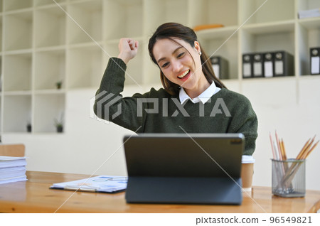 Cheerful Asian businesswoman happy with her work project, showing clenched fists, celebrating Cheerful Asian businesswoman happy with her work project, showing clenched fists, celebrating 96549821