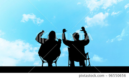 Silhouette of two men and women sitting on outdoor chairs and raising their hands_wide 96550656