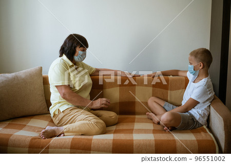 Mature woman and boy wearing masks on sofa, quarantine communication concept. Mature woman and boy wearing masks on sofa, quarantine communication concept. 96551002