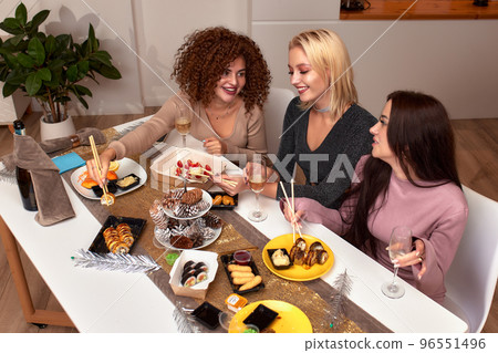Discussing the latest gossips. Three beautiful young women talking and smiling while drinking wine and sitting on the couch together Discussing the latest gossips. Three beautiful young women talking and smiling while drinking wine and sitting on the couch together 96551496