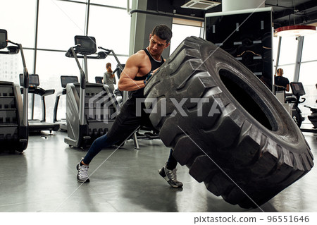 Muscular fitness man moving large tire in gym center, concept lifting, workout training. 96551646