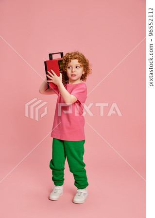 Portrait of cute little girl, child with curly red hair posing with music player isolated over pink background Portrait of cute little girl, child with curly red hair posing with music player isolated over pink background 96552112