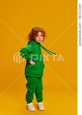 Portrait of cute little girl, child with curly red hair posing in green costume isolated over yellow background 96552164