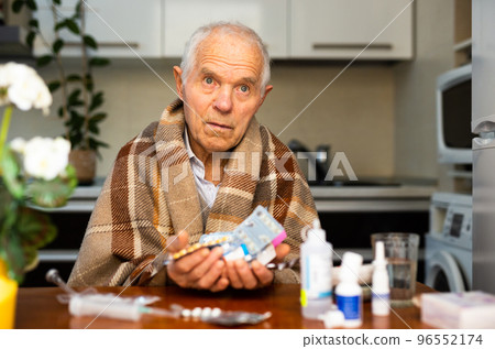 gray haired elderly man with handful of different medications in hand at home 96552174