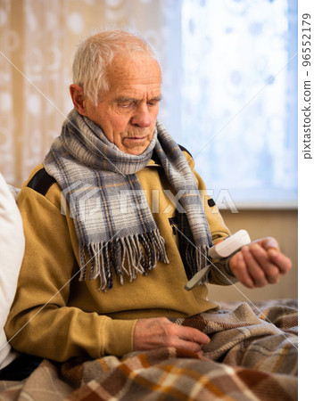 gray haired elderly man measuring pressure with tonometer at home 96552179