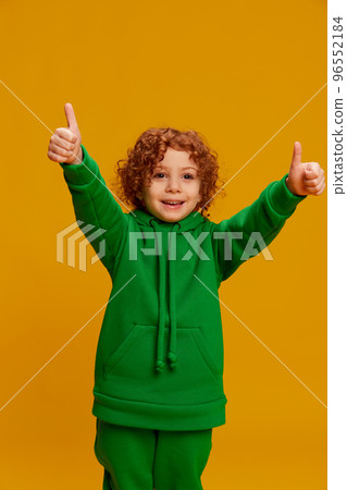 Portrait of cute little girl, child with curly red hair posing, showing cheerful emotions isolated over yellow background 96552184