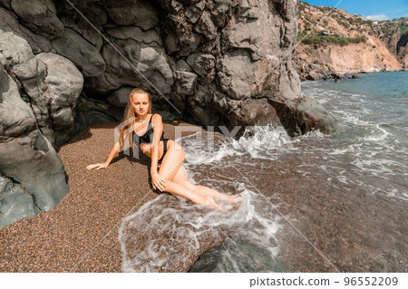 Woman swimsuit sea. Attractive blonde woman in a black swimsuit enjoying the sea air on the seashore around the rocks. Travel and vacation concept. 96552209