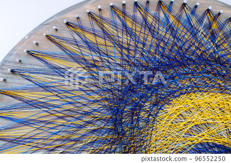 Colored thread mandala on a wooden board with nails. Mandala Moon Harmony Sun esotericism and psychology pictures from yellow and blue silk threads. 96552250