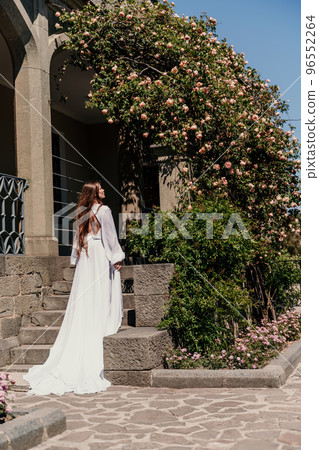 a beautiful woman in a white flowing long dress stay near a beautiful field with pink flowers rear view a beautiful woman in a white flowing long dress stay near a beautiful field with pink flowers rear view 96552264