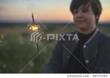 A cute boy holds sparklers in his hands, fireworks in the evening in the summer at sunset. Festive mood A cute boy holds sparklers in his hands, fireworks in the evening in the summer at sunset. Festive mood 96553569