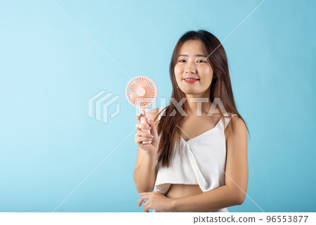 Asian beauty young woman holding pink portable electric mini fan near her face studio shot isolated on blue background, Female hand hold small plastic fan handheld she enjoying cool wind blowing Asian beauty young woman holding pink portable electric mini fan near her face studio shot isolated on blue background, Female hand hold small plastic fan handheld she enjoying cool wind blowing 96553877