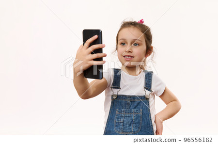 Happy adorable Caucasian little child girl using mobile phone, talks with her parent via video link, isolated over white background with copy space for advertising text. Online chat on smartphone 96556182