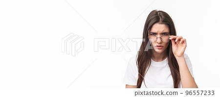 Close-up portrait of suspicious young serious-looking woman, look from under glasses, squinting at person with judgemental disbelief stare, standing white background, have doubts 96557233