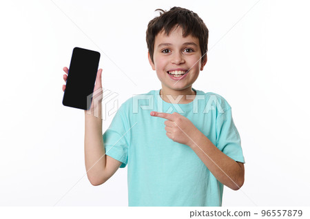 Wow awesome mobile app. Handsome Caucasian teenage boy points at smartphone with black blank screen with copy space for young advertising text, smiles looking at camera, posing over white background Wow awesome mobile app. Handsome Caucasian teenage boy points at smartphone with black blank screen with copy space for young advertising text, smiles looking at camera, posing over white background 96557879