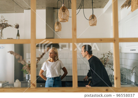 Remote view of angry husband scolding, raising voice, yelling at ignoring young girlfriend wife standing in kitchen room. Young Caucasian couple quarrelling yelling at home. Concept of family problems 96558037