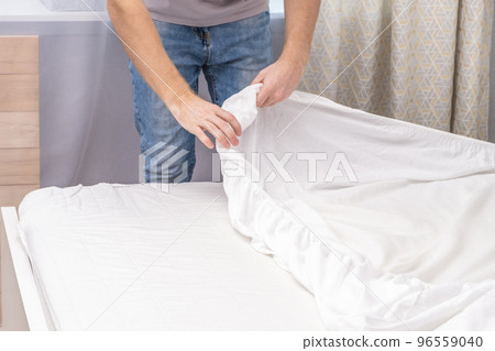 A man makes his cozy bed with fresh bright white 96559040
