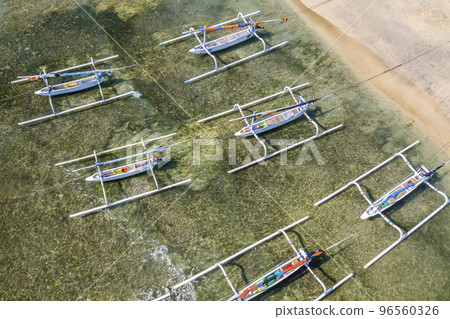 A top-down view of a group of traditional Balinese fishing boats moored to shore. Boats with additional beams on the sides against the backdrop of green ocean water in shallow water 96560326