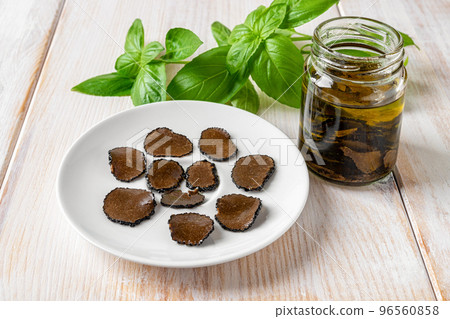 Truffle carpaccio slices on a plate and jar of sliced black truffle in oil over white wooden table. 96560858