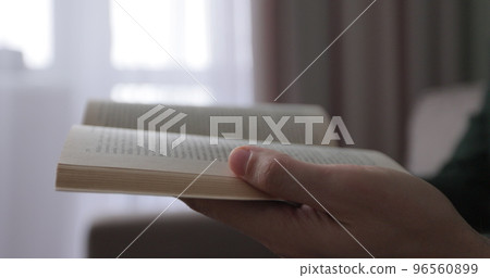 Young man read book while sitting on a sofa at home. Close up at book in hands. 96560899