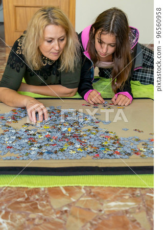 Mother and daughter lying on the floor doing a puzzle together while having a nice time on a girls night out. 96560958