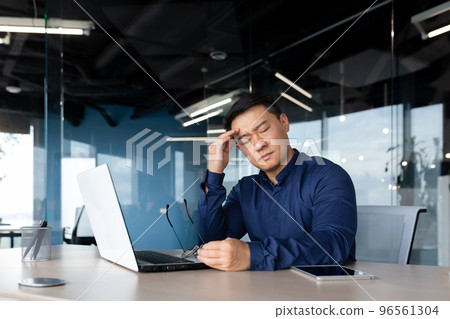 thinking sad asian man with closed eyes working in office indoors, businessman sitting at desk overworked and frustrated, mature man upset with achievement results. 96561304