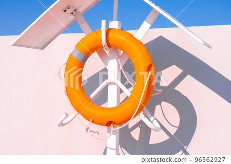 Orange lifebuoy on beach by sea. Safety equipment for rescuing people on seashore. Orange lifebuoy on the pier of blue sky and azure sea Orange lifebuoy on beach by sea. Safety equipment for rescuing people on seashore. Orange lifebuoy on the pier of blue sky and azure sea 96562927