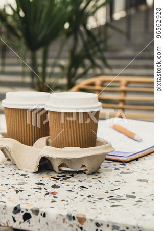 Two paper cups with lid for tea to go. Coffee take away on the table. Take-out coffees with brown paper cup holder. Brown safety cardboard collars. Cardboard tray Two paper cups with lid for tea to go. Coffee take away on the table. Take-out coffees with brown paper cup holder. Brown safety cardboard collars. Cardboard tray 96562928