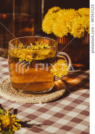 Dandelion flower healthy tea in glass teapot and glass cup on table. Delicious herbal Hot tea from fresh dandelion flowers at home at summer day. Green clearing. Bouquet of dandelions petals Dandelion flower healthy tea in glass teapot and glass cup on table. Delicious herbal Hot tea from fresh dandelion flowers at home at summer day. Green clearing. Bouquet of dandelions petals 96563128