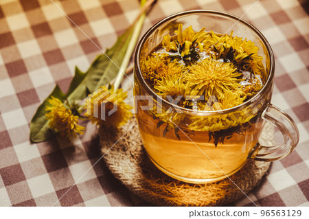 Dandelion flower healthy tea in glass cup on table. Herbal medicine Delicious tisane tea from with fresh yellow blossom dandelion flowers inside tea cup. Green clearing infusion Wildflowers Eco 96563129
