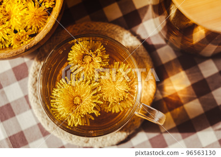 Dandelion flower healthy tea in glass teapot and glass cup on table. Delicious herbal Hot tea from fresh dandelion flowers at home at summer day. Green clearing. Bouquet of dandelions petals 96563130
