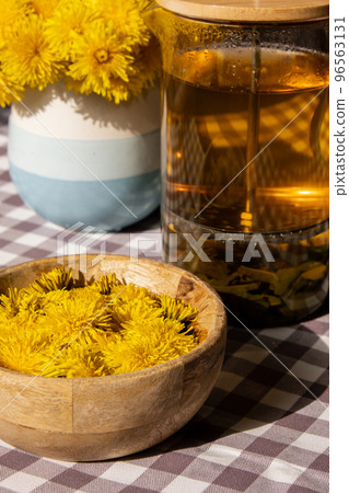 Preparing Dandelion flower healthy tea in glass cup on table. Herbal medicine Delicious tisane tea from with fresh yellow blossom dandelion flowers inside tea cup. Green clearing infusion Wildflowers Preparing Dandelion flower healthy tea in glass cup on table. Herbal medicine Delicious tisane tea from with fresh yellow blossom dandelion flowers inside tea cup. Green clearing infusion Wildflowers 96563131