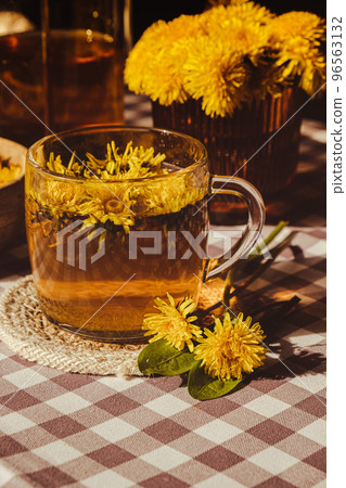 Dandelion flower healthy tea in glass teapot and glass cup on table. Delicious herbal Hot tea from fresh dandelion flowers at home at summer day. Green clearing. Bouquet of dandelions petals Dandelion flower healthy tea in glass teapot and glass cup on table. Delicious herbal Hot tea from fresh dandelion flowers at home at summer day. Green clearing. Bouquet of dandelions petals 96563132