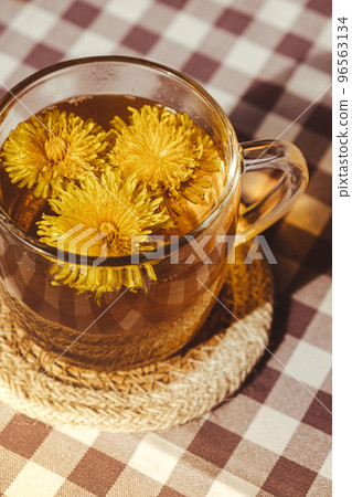 Dandelion flower healthy tea in glass cup on table. Herbal medicine Delicious tisane tea from with fresh yellow blossom dandelion flowers inside tea cup. Green clearing infusion Wildflowers Eco Dandelion flower healthy tea in glass cup on table. Herbal medicine Delicious tisane tea from with fresh yellow blossom dandelion flowers inside tea cup. Green clearing infusion Wildflowers Eco 96563134