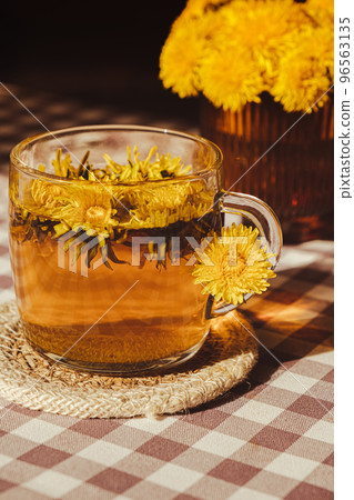 Dandelion flower healthy tea in glass cup on table. Herbal medicine Delicious tisane tea from with fresh yellow blossom dandelion flowers inside tea cup. Green clearing infusion Wildflowers Eco Dandelion flower healthy tea in glass cup on table. Herbal medicine Delicious tisane tea from with fresh yellow blossom dandelion flowers inside tea cup. Green clearing infusion Wildflowers Eco 96563135