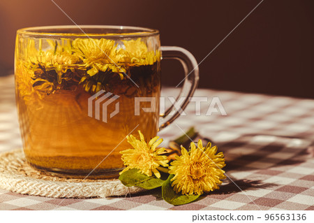 Dandelion flower healthy tea in glass cup on table. Herbal medicine Delicious tisane tea from with fresh yellow blossom dandelion flowers inside tea cup. Green clearing infusion Wildflowers Eco Dandelion flower healthy tea in glass cup on table. Herbal medicine Delicious tisane tea from with fresh yellow blossom dandelion flowers inside tea cup. Green clearing infusion Wildflowers Eco 96563136